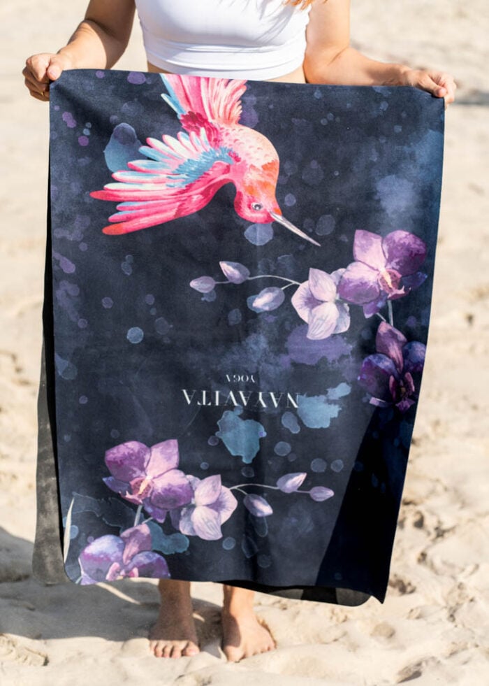 žena na pláži stojí a drží napůl přeloženou černou ultralehkou skládací podložku na cvičení Colibri NAYAVITA Yoga