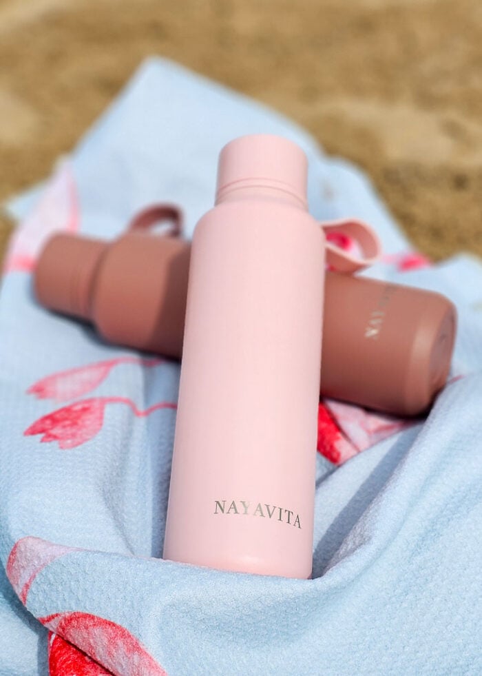 Na plážové osušce leží 2 vakuově izolované láhve na vodu NAYAVITA v růžové a terracotta barvě